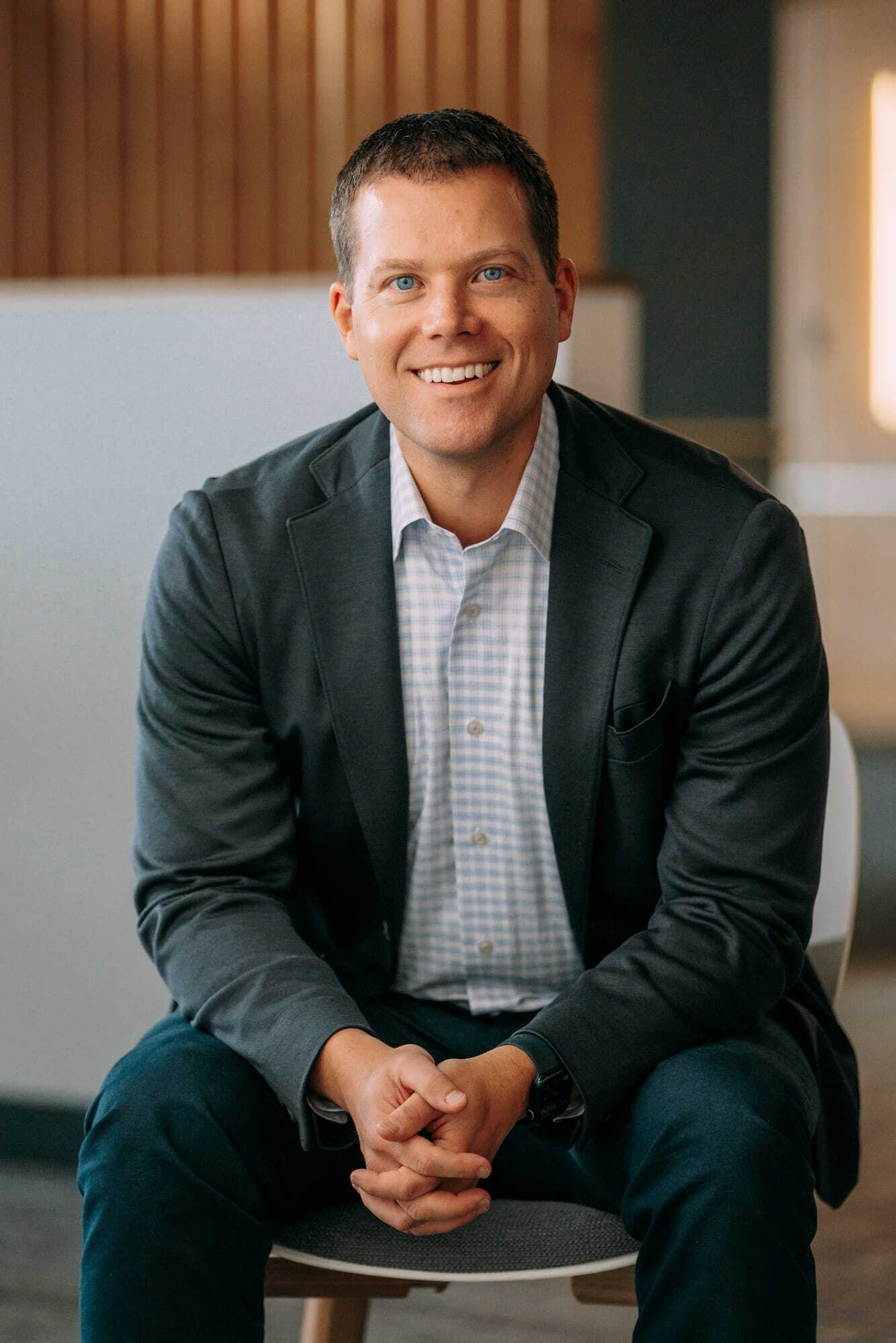 Smiling man in a blazer and light shirt seated in a modern office setting.