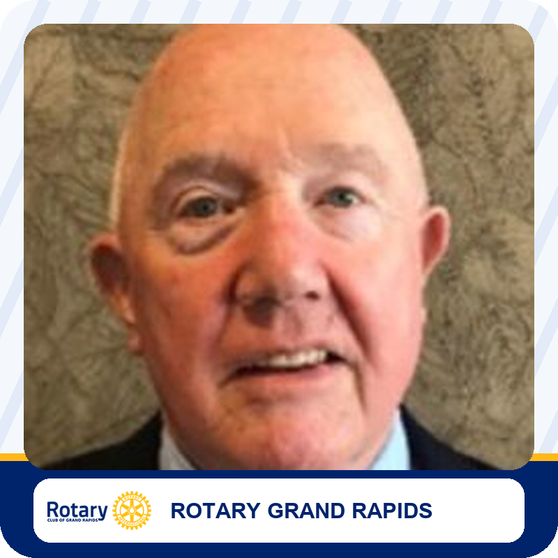 Close-up portrait of an older man in a suit, against a textured background, with Rotary Grand Rapids branding below