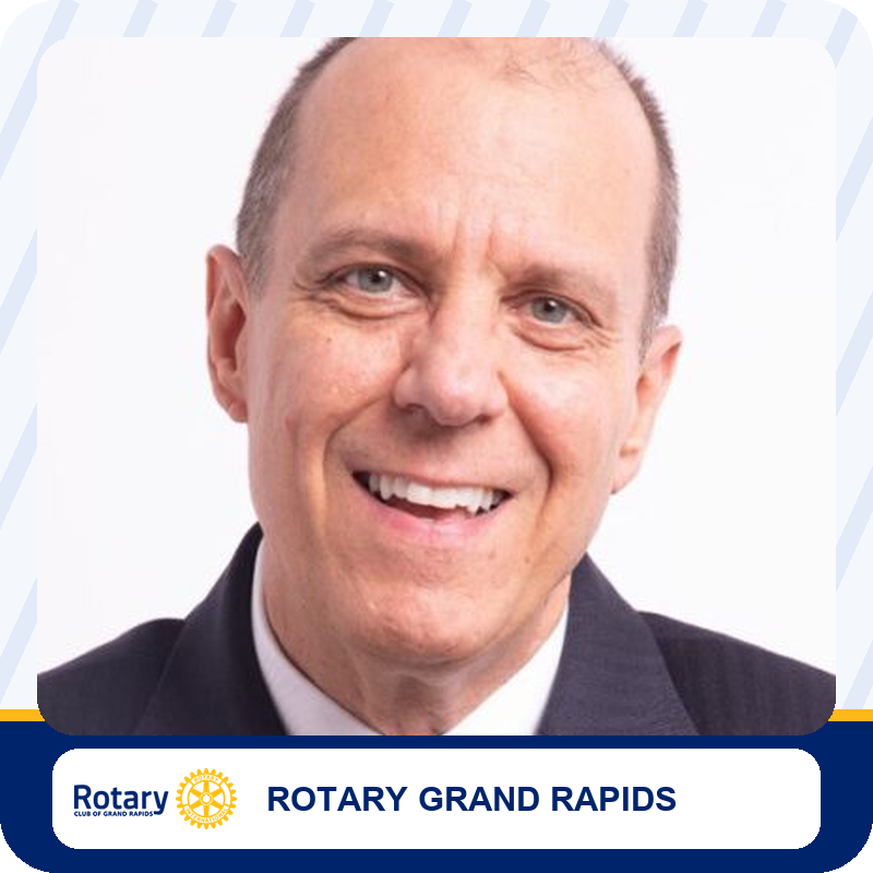 Smiling man in a dark suit with Rotary Grand Rapids branding below.