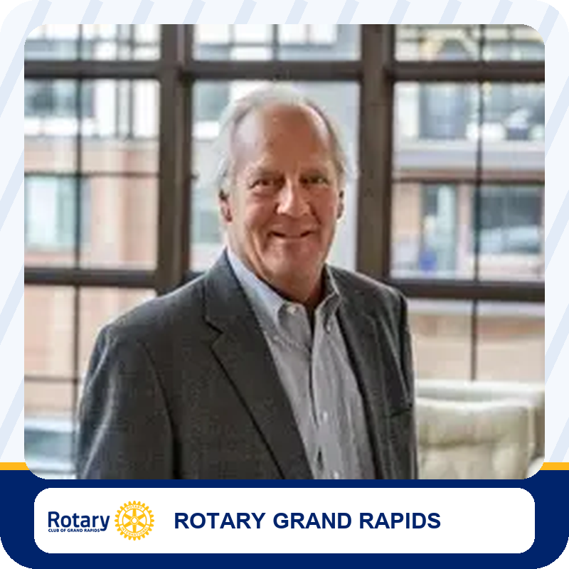 Smiling man in a dark suit and light shirt standing indoors, a Rotary Grand Rapids member portrait.
