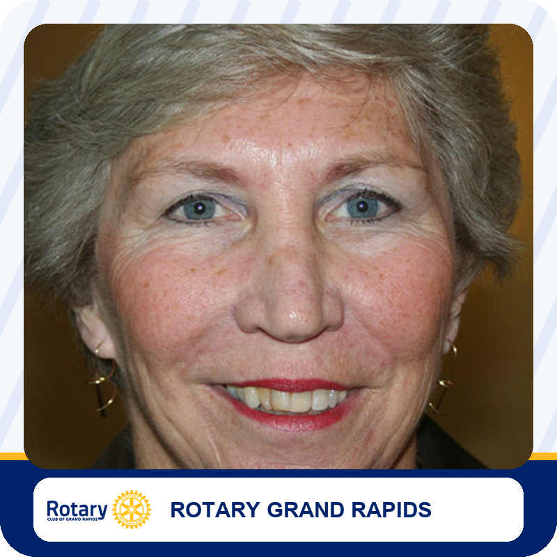 mj-foundation-leadership Close-up portrait of a smiling older woman with short gray hair and blue eyes on a Rotary Grand Rapids banner.