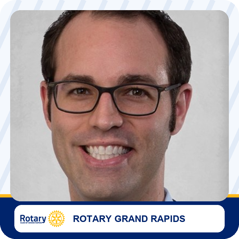 neil-marchand Smiling man with short dark hair and rectangular glasses in a head-and-shoulders portrait against a gray backdrop; Rotary Grand Rapids branding appears below.