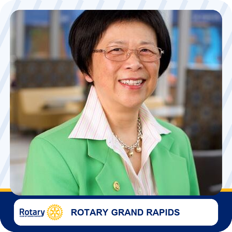 ping-liang Portrait of a smiling woman wearing a green blazer and striped shirt, in a Rotary Grand Rapids setting.