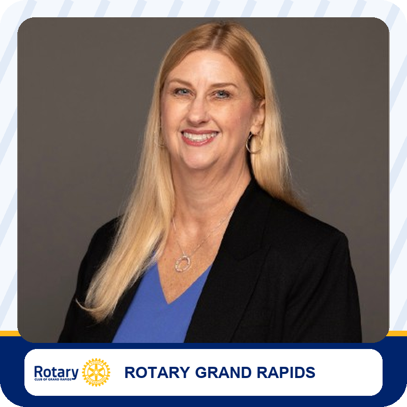Professional headshot: smiling blonde woman in a blue top and black blazer, Rotary Grand Rapids representative.