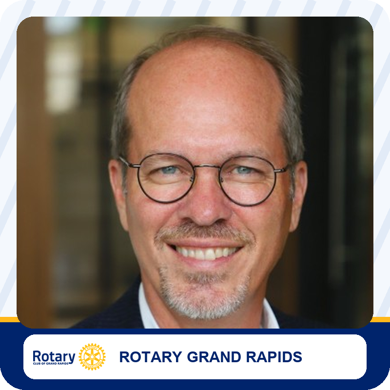 Smiling man with round glasses and light facial hair, wearing a dark blazer; used for Rotary Grand Rapids branding.