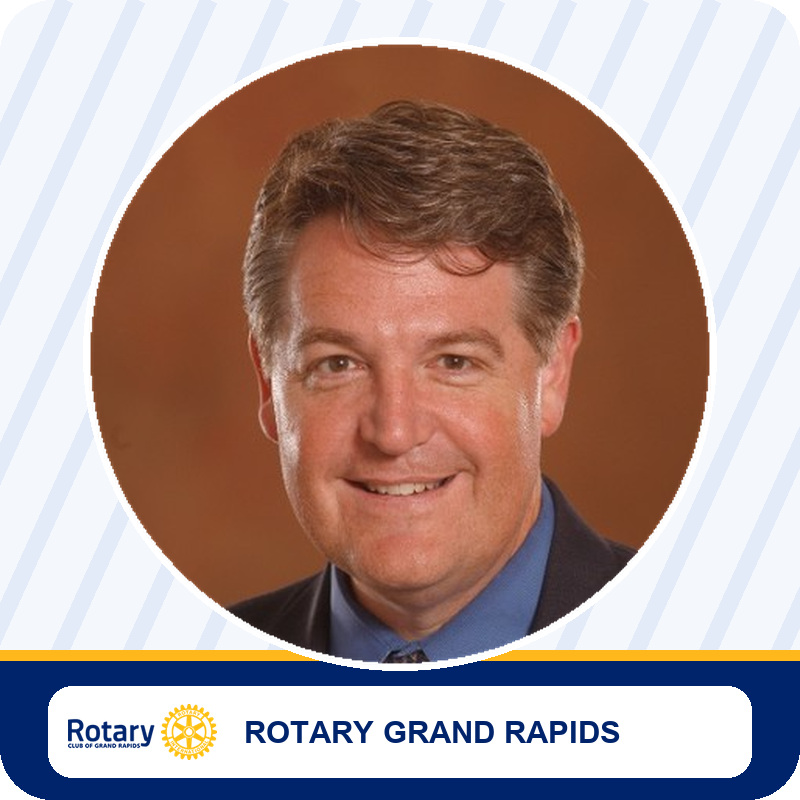 Portrait photo of a smiling man in a dark suit and blue shirt, circle-cropped image with a Rotary Grand Rapids banner below.