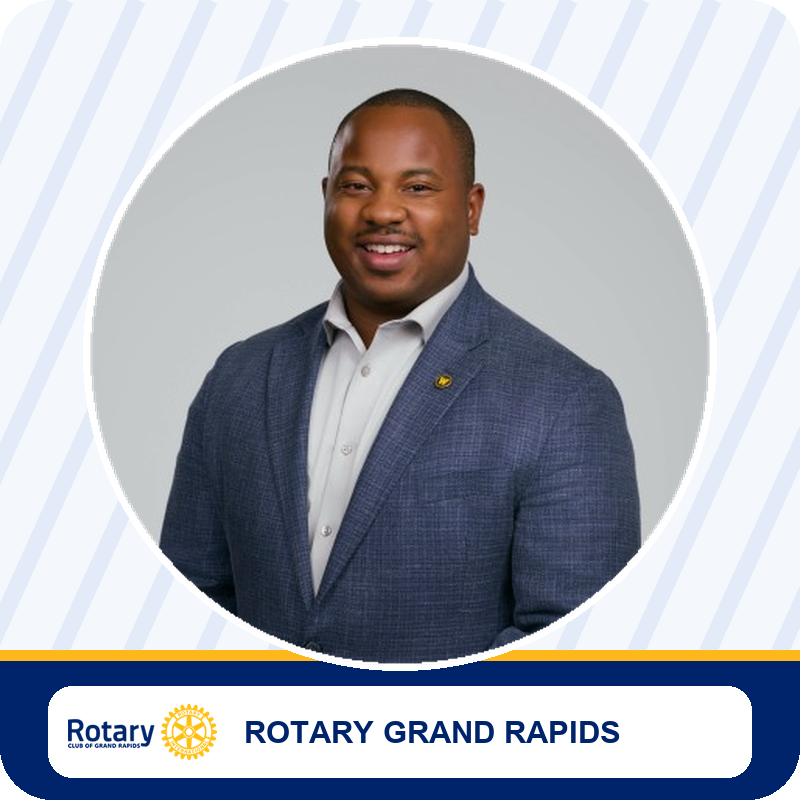 Smiling man in a navy blazer and white shirt, circular portrait with Rotary Grand Rapids branding in the foreground.